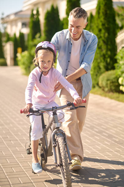 istock A man supporting a girl while she riding a bike 1354918052