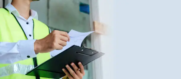 home inspector engineer in green reflective jacket checking review document and inspecting with clipboard at construction site building interior, construction, contractor and engineering concept