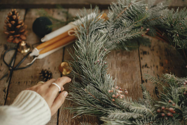 istock Rustic christmas wreath with pine branches and red berries in snow and hand with stylish rings on rustic old wooden background close up. Atmospheric winter holidays in countryside 1354926257