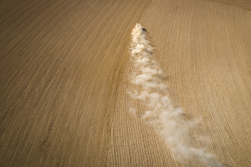 Tractor, harrow and dust on an agricultural field - aerial view