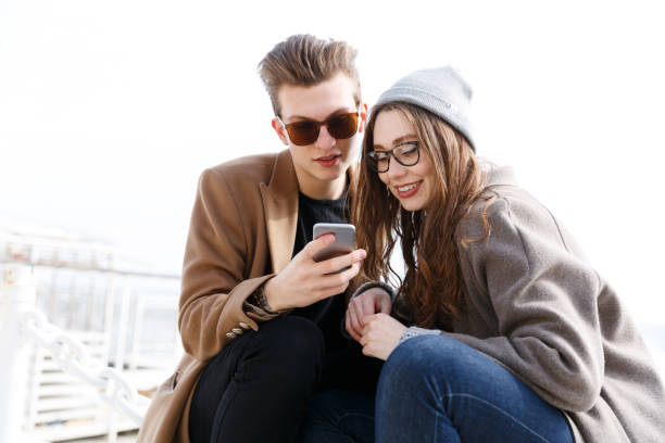 istock Couple using mobile phone together on the beach in autumn 1354928967