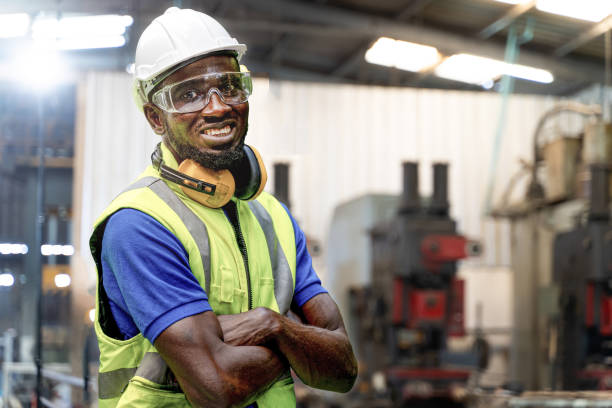 istock African man workers engineering standing with confident with blue working suite dress and safety helmet in front of indoor factory. Concept of smart industry worker operating. 1354930125