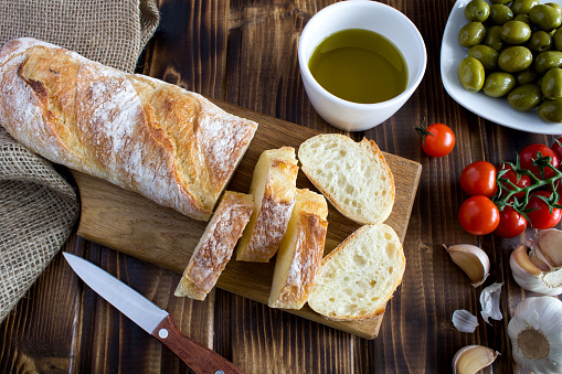 Fresh italian baguette, green olive  and olive oil on the  rustic wooden background. Top view. Close-up.