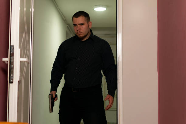 akční portrét vážného mladého detektiva, zvláštního agenta muže držícího zbraň mířící na zbraň, zapojeného do střelby, vstupujícího do bytu s opatrností, hledajícího zločince. - bránění fotky - stock snímky, obrázky a fotky