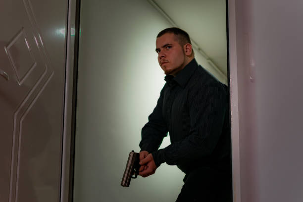 Action portrait of serious young detective, special agent man holding gun pointing the weapon, involved in shooting, entering in the apartment with caution, looking for criminals. HD stock photographyof a action portrait of serious young detective, special agent or a a hitman, man holding gun pointing the weapon, involved in shooting, entering in the apartment with caution, looking. gunman stock pictures, royalty-free photos & images