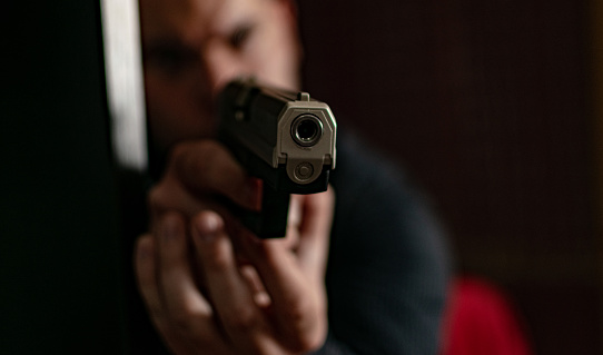 HD stock photographyof a action portrait of serious young detective, special agent or a a hitman, man holding gun pointing the weapon, involved in shooting, entering in the apartment with caution, looking.