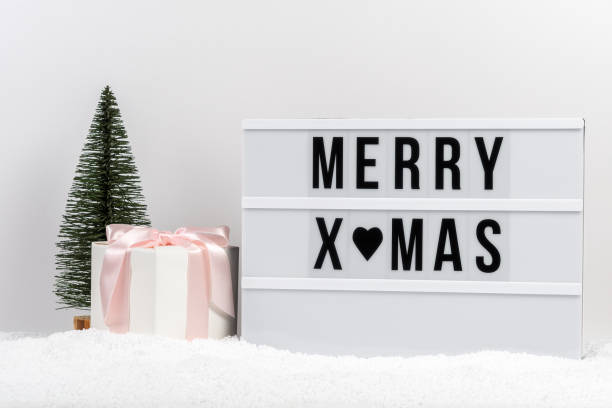 istock Christmas tree, gift box and lightbox with text MERRY XMAS on a table with snow. Minimal Christmas or New Year concept. 1354935899