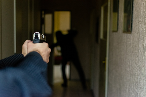 Action portrait of serious young detective, special agent, holding gun pointing the weapon, involved in shooting, entering in the the hallway in some bulding with caution, looking for and arresting a criminal.