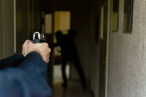 Photo of HD stock photographyof a action portrait of serious young detective, special agent, holding gun pointing the weapon, involved in shooting, entering in the the hallway in some bulding with caution, looking for and arresting a criminal.