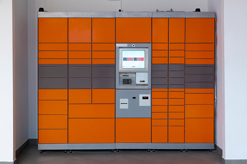 Front view of orange automated post terminal (also known as packstation, smart locker or postamat) standing in a niche against the wall. 24-7 self-service post office without employees. Vending theme.