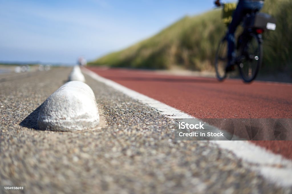 Bicycle path in South Holland. Part of a male dark clothed cyclist depth of field. Big beach dune with grass. Netherlands, Schouwen-Duiveland, Brouwersdam. Asphalt Stock Photo