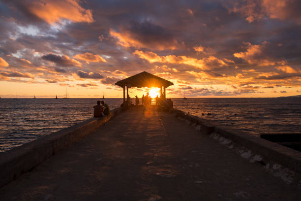 Oahu, USA - Oct 31, 2021: Locals and tourists watching the sunset off the Waikiki Wall pier off the Queens Beach.