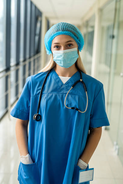 young nurse in uniform mask with mittens with stethoscope stands in hospital stock photo