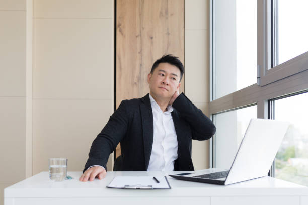 istock young asian office worker suffering from headache at work in the office drinks medicine pill with water. Sick man in a suit at the computer indoors with severe pain ache uses the drug in workplace 1354940113