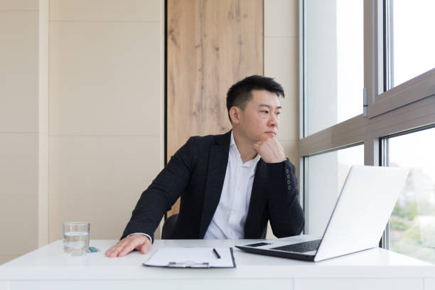 istock young asian office worker suffering from headache at work in the office drinks medicine pill with water. Sick man in a suit at the computer indoors with severe pain ache uses the drug in workplace 1354940117