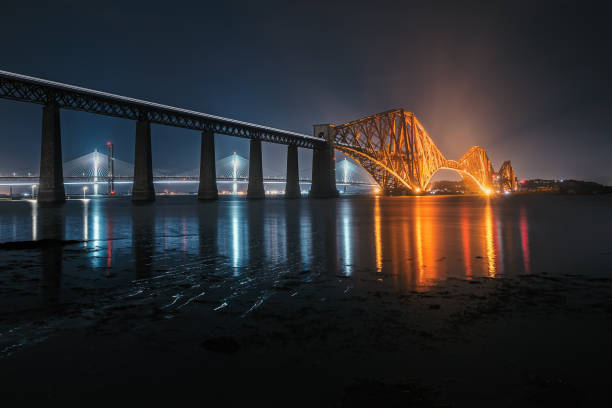 View of Forth Rail Bridge at night and and the glow trail of a moving train over the sea stock photo
