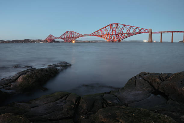 View of Forth Rail Bridge in the evening and the rocky coast in the foreground stock photo