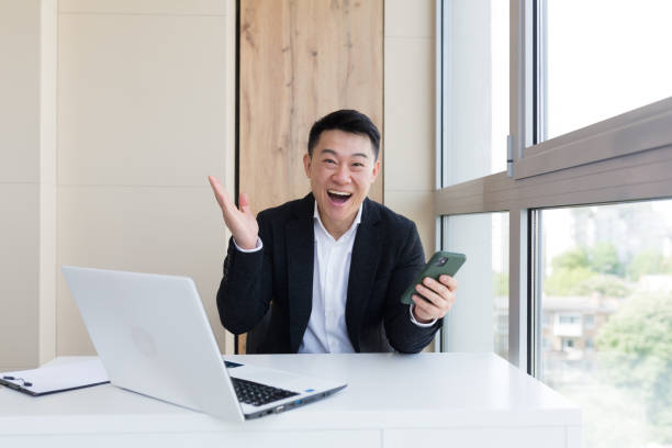 Happy young Asian business man in office, looking at camera, with emotions of winner or victory, financial promotion sports betting. The man exclaims happily while playing the game. Excited with joy, celebrating success feliz joven hombre de negocios asiático en el cargo, mirando a la cámara, con emociones de ganador o victoria, promoción financiera apuestas deportivas. el hombre exclama felizmente mientras juega el juego. emocionado de alegría, celebrando el éxito