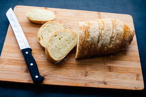 Sliced French bread on a wooden cutting board with a bread knife