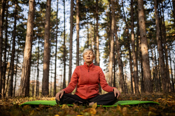 Senior woman practicing yoga workout routine in park with eyes closed stock photo