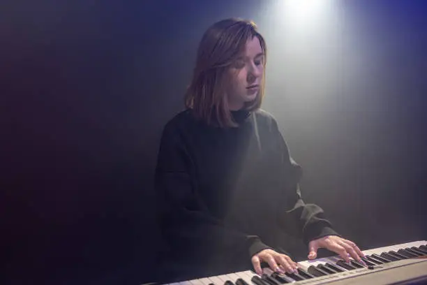 Young woman pianist in black plays the keys in a dark room with a haze, music performer, performance, live music concert, copy space.