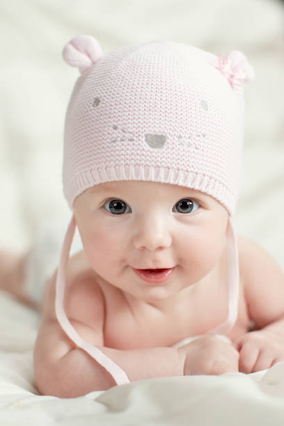 neonata in cappello a maglia rosa su un letto - baby sleeping bedding teddy bear foto e immagini stock