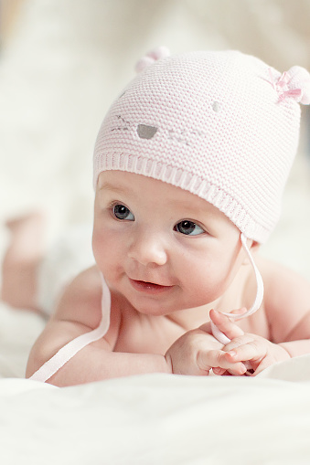 Newborn baby girl in pink knitted hat on a bed.
