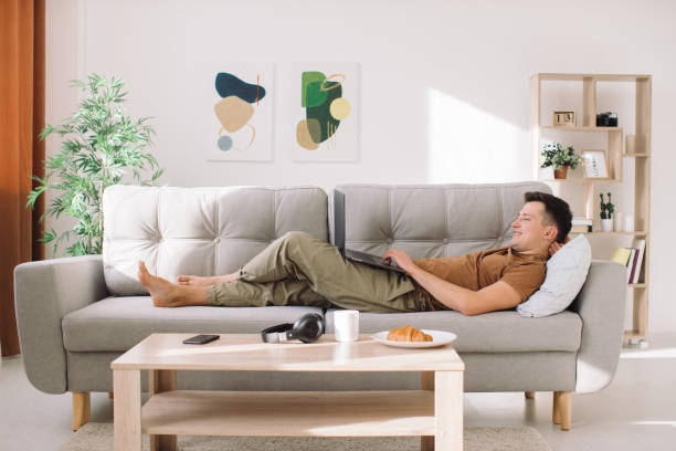istock Handsome man lying on sofa and working on his laptop