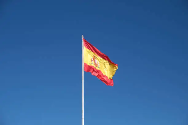 Spanish flag flying on blue sky.