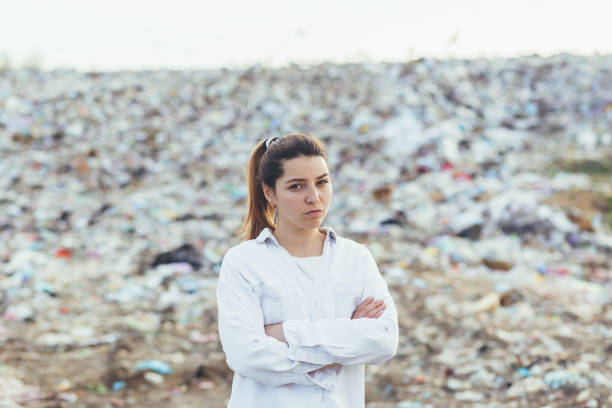 angry woman standing in a landfill, dissatisfied with the scale of environmental pollution looking into the camera - toxic substance spilling pouring bottle imagens e fotografias de stock