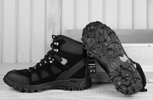 Close-up pair black textile work boots for safe winter with steel toe,boot view of non-slip material sole on gray wooden background and metal tool box.Comfort flexibile safety workers concept,roofer.