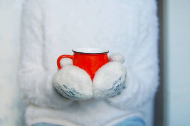 Red mug in two hand in mittens. Jeanse and white sweater