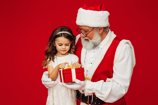 A cute little girl sitting on Santa Claus' lap and holding a gift