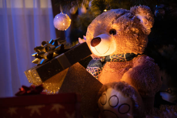 istock Teddy bear holding a gift box with glowing light under a Christmas tree in the dark. 1354955523