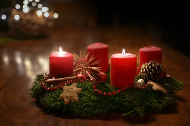 Photo of Second Advent - decorated Advent wreath from fir branches with red burning candles on a wooden table in the time before Christmas, festive bokeh in the warm dark background, copy space, selected focus