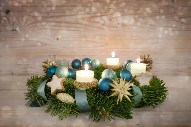 Advent wreath series number three with lit candles, blue Christmas baubles and decoration on a rustic wooden snowy background, fourth Sunday, copy space, selected focus, narrow depth of field