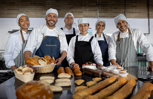 Portrait of a happy group of Latin American bakers working at a bakery making bread and looking at the camera smiling