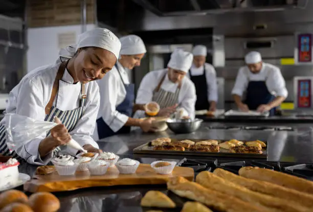Happy team of Latin American people working at a bakery making pastries and smiling - food and drinks concepts