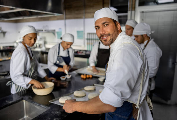 istock Happy baker making bread at the bakery with his team 1354962836