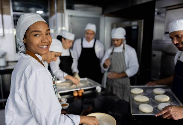 istock Happy baker making bread at the bakery with a team of workers 1354962838