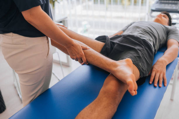 Female physiotherapist bending the knee of an injured male patient lying on a massage bed in the clinic Shot of a young man visiting his physiotherapist for a rehabilitation session sports medicine stock pictures, royalty-free photos & images