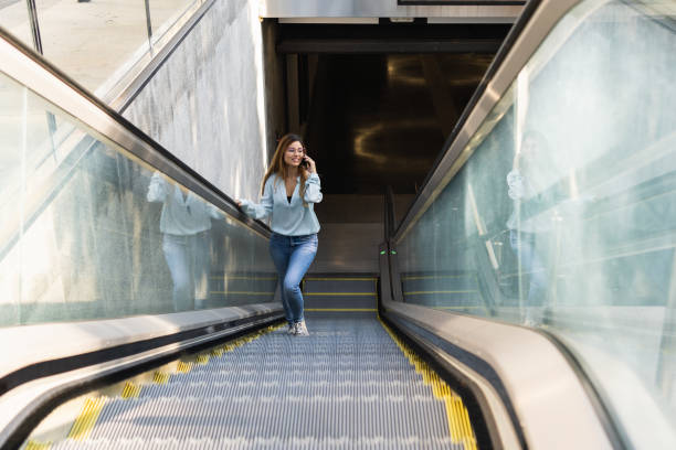 istock Attractive businesswoman with glasses using smartphone while smiling, going up on metro, subway, airport escalator. Business concept 1354974612