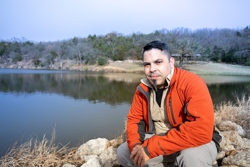 Man alone standing in front of a lake with an orange coat.