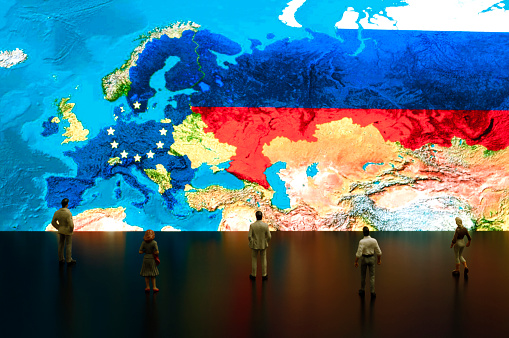 Businessman/politician figurines examine satellite view European Union and Russia maps.