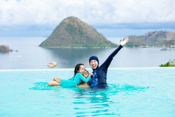 Asian  Muslim family enjoy swimming at the pool with sea at the background asian family enjoy swimming at the pool with sea at the backgroud family beach vacations travel stock pictures, royalty-free photos & images