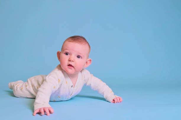 istock Infant baby boy looks with curiosity while lying on his tummy, studio blue background. Four month old child, copy space 1354989887