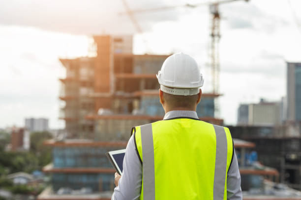 istock Asian engineer handsome man or architect use tablet with white safety helmet in city construction site . Standing on rooftop building construction at capita 1354994672
