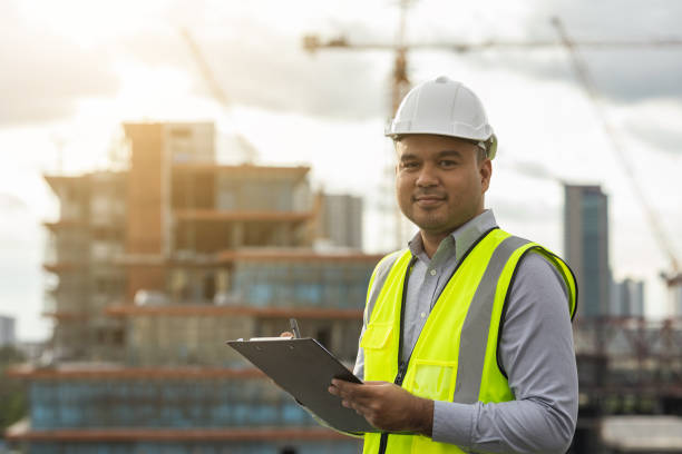 istock Inspector engineer man or architect with clipboard with white safety helmet in city construction site. Checking with checklist on rooftop building construction at capital. 1354994674