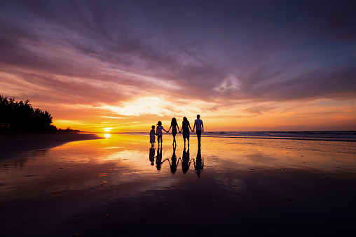 Silhouettes of happy family holding the hands on beach during sunset