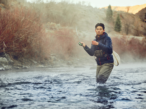 An Asian Korean man, fly fishing on the Provo River in Utah during winter.